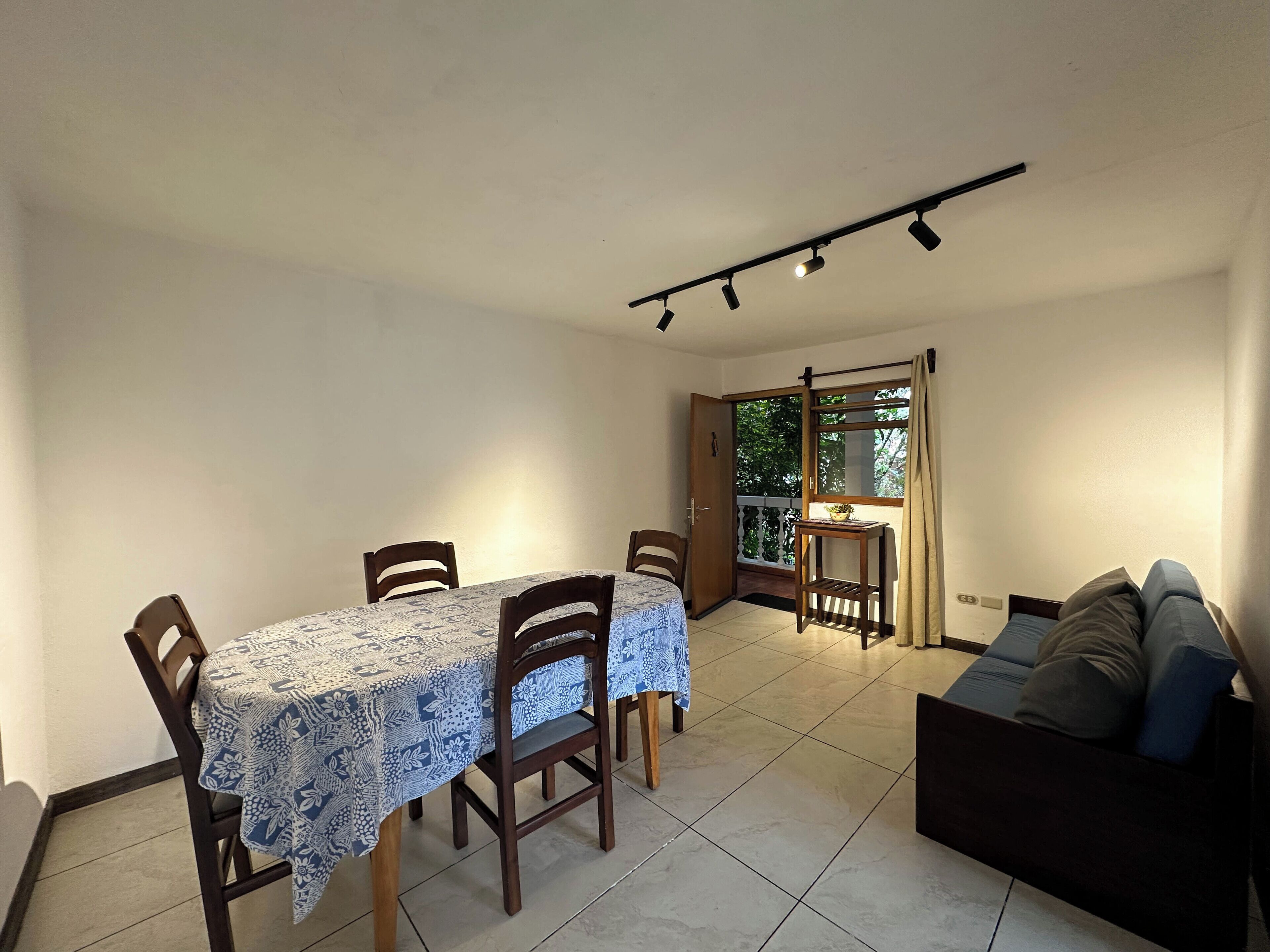 A dining area with a table and chairs, a sofa, and a balcony with a view.