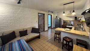 A compact living space with a sofa, a kitchen area, and a dining table. - Apartamentos Otorongo (Cuenca)