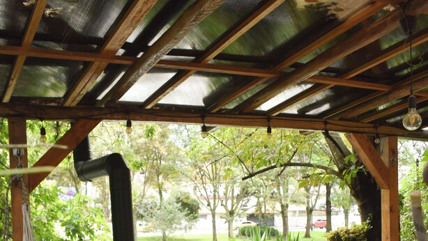 A hammock under a wooden pergola with a view of a garden and a table with a striped tablecloth. - Apartamentos Otorongo (Cuenca)