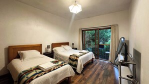 A hotel room with two beds, a large sliding glass door to a balcony, a desk with a computer, and a ceiling light. - Apartamentos Otorongo (Cuenca)