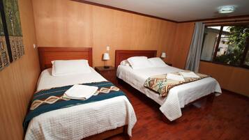 A hotel room with two beds, wooden flooring, and a window with a view.