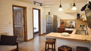 A kitchen with a refrigerator, stove, and sink. There is a wooden door and a white wall. - Apartamentos Otorongo (Cuenca)