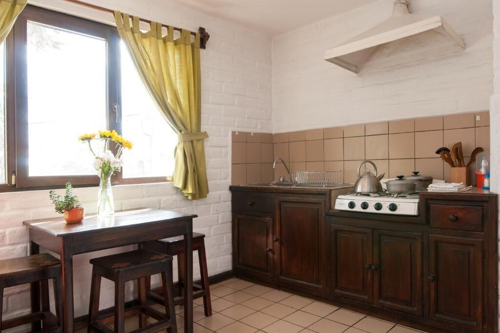 Una cocina con mesa de madera, taburetes, estufa y ventana con cortinas.