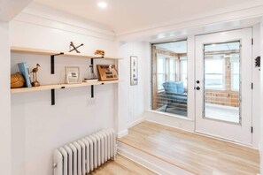 A room with a wooden floor, a radiator, a door with a glass panel, and a shelf with various items.