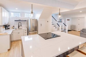 A modern kitchen with white cabinetry, a large island, stainless steel appliances, and pendant lighting. - The Granite Harbor (Wells)