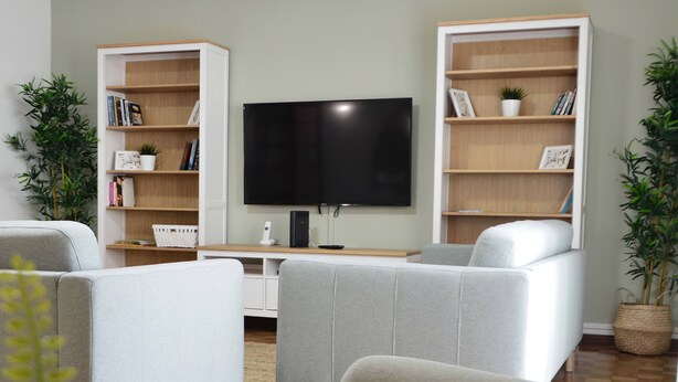 A living room with a flat-screen TV, two white sofas, and wooden bookshelves. - Old Village Hostel (Ponte de Lima)