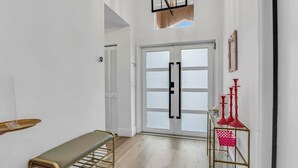 Un pasillo con un banco, una mesa de vidrio y candelabros rojos, y una puerta con paneles de vidrio esmerilado.