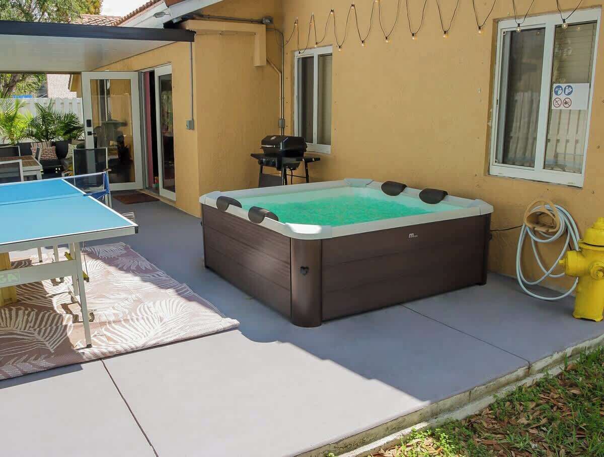 A hot tub in a covered outdoor area with a table and chairs nearby.