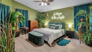 Un dormitorio con cama, ventilador de techo, letrero de neón y varias plantas.