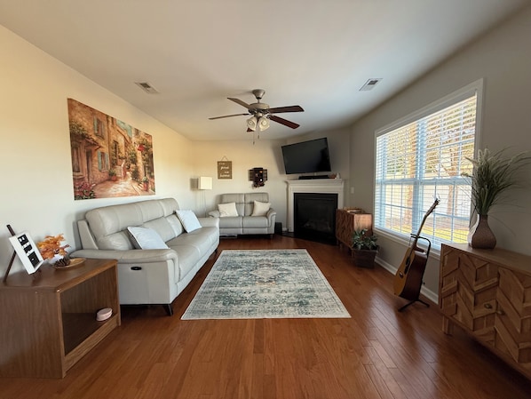 A living room with a sofa, a fireplace, a television, and a large window with blinds.