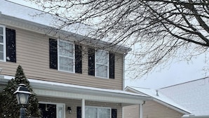 Une maison à deux étages avec un porche abrité et une pelouse recouverte de neige.