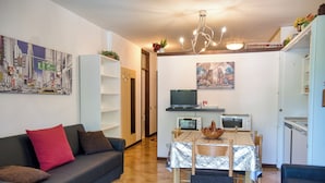 A living room with a sofa, a dining table with chairs, a TV, and a kitchen area with a microwave. - Top Panorama - Piscina (Introbio)