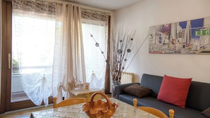A living room with a sofa, a table with a woven basket, a cityscape painting, and a window with sheer curtains. - Top Panorama - Piscina (Introbio)