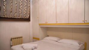 A hotel room with a bed, white linens, a radiator, and a wardrobe with yellow accents. - Top Panorama - Piscina (Introbio)