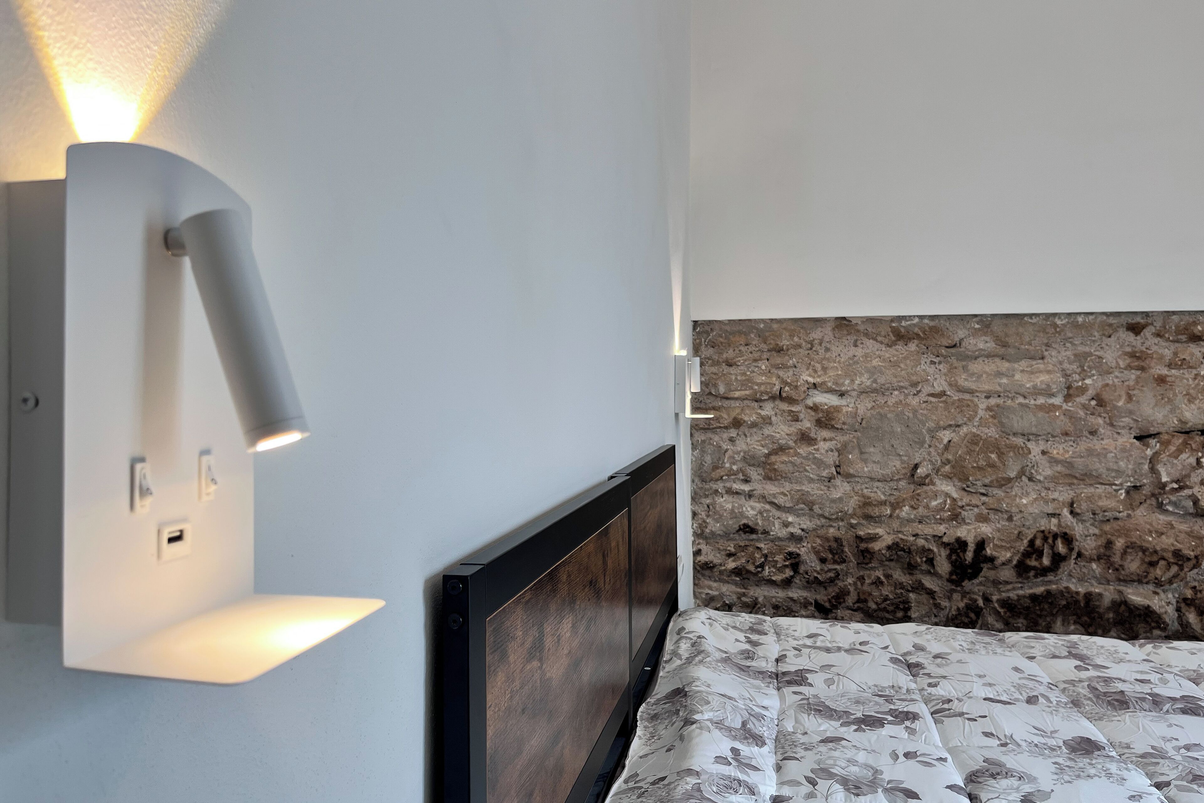 A bedroom with a bed, a wall-mounted light fixture, and a stone accent wall.