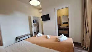 A hotel room with a bed, a TV mounted on the wall, and a bathroom visible through an open door.