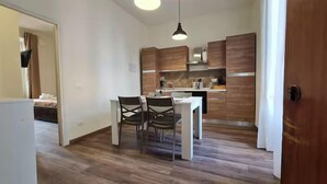 A compact kitchen with wooden cabinets, a white countertop, and a dining area with two chairs.