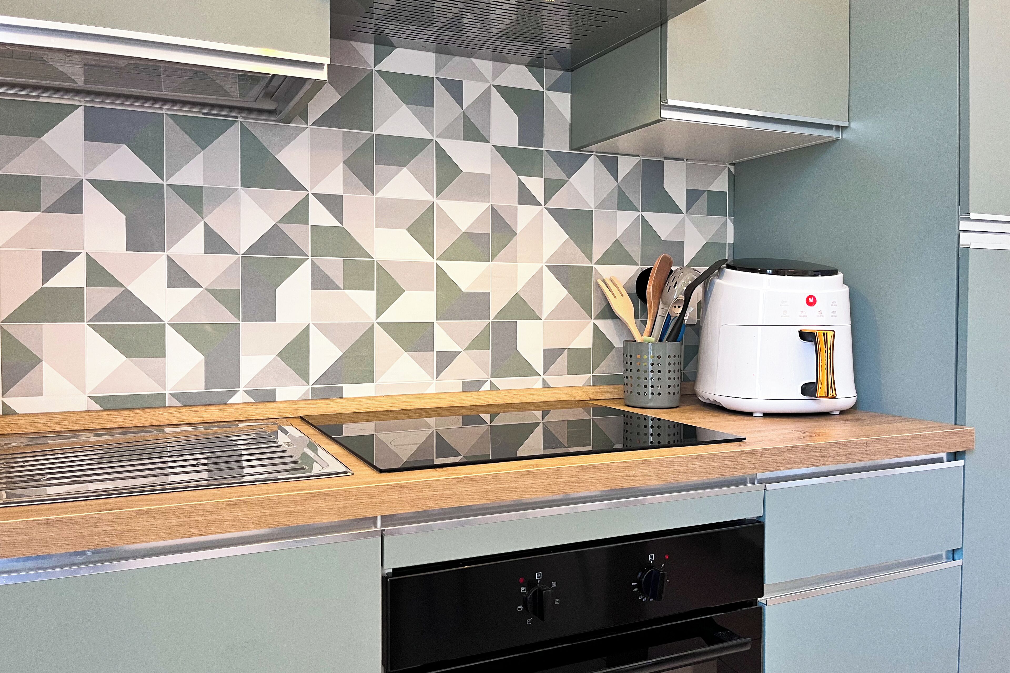 Una cocina moderna con un salpicadero geométrico, estufa integrada y una cafetera sobre la encimera.