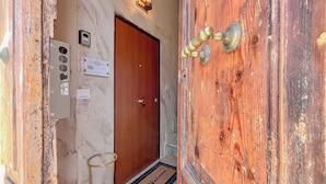 A wooden door with a brass handle, a doormat with "Welcome" text, a wall-mounted light fixture, and a sign reading "Cellia Traiani".