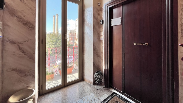 A hotel entrance with a dark wooden door, a glass door leading to a balcony with a red railing, and a marble wall.