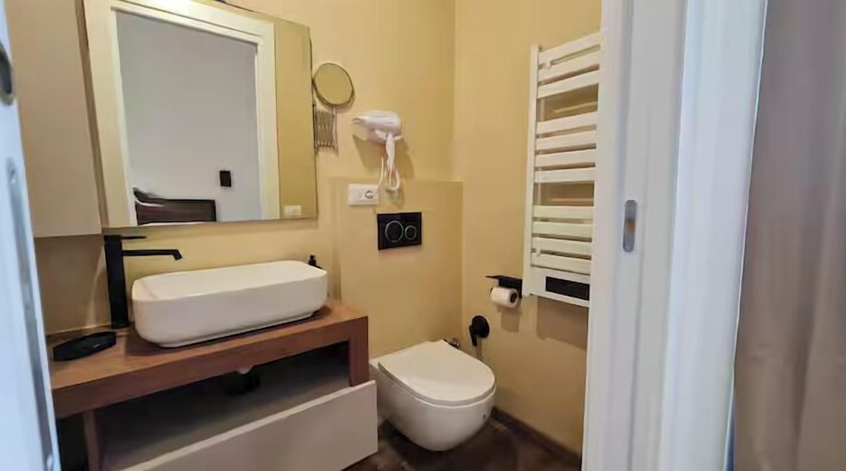 Un baño con lavamanos blanco, inodoro, toallero y espejo.