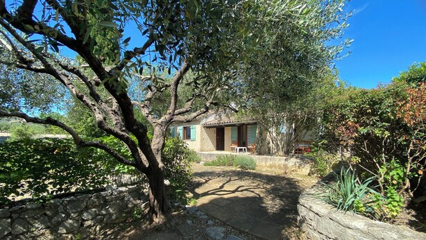 A stone-walled courtyard with a rustic house, a stone pathway, and lush greenery.
