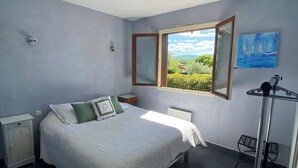 A bedroom with a bed, a nightstand, a radiator, a window with a view, and a painting on the wall.