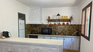 A kitchen with a white countertop, a microwave, a stove, and a sink. There are cabinets and a window above the sink.