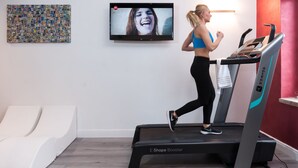 A person running on a treadmill in a room with a TV displaying a program, a wall art piece, and a red accent wall.