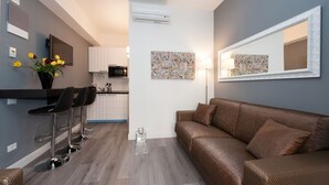 A modern living room with a brown sofa, a coffee table, and a kitchen area with a microwave and cabinets.