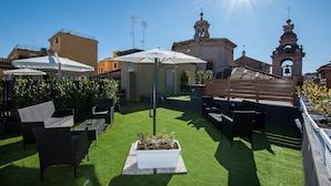 A rooftop patio with outdoor furniture, a white umbrella, and a view of a historic building with a bell tower.