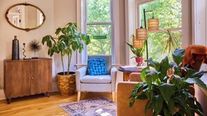 A cozy living room with a wooden cabinet, a blue cushioned chair, and various plants. - A chic second-floor plant-filled retreat in Chicago's Logan Square neighborhood. (Chicago)
