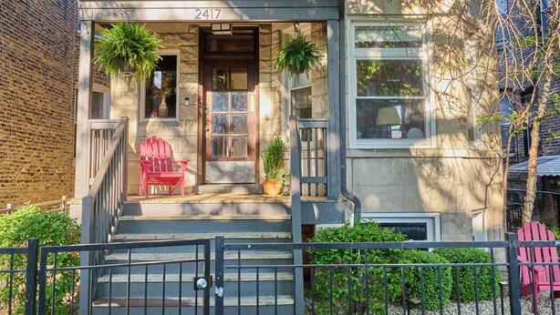 A two-story house with a stone facade, a front porch with a red chair, and a number "2417" on the door. - A chic second-floor plant-filled retreat in Chicago's Logan Square neighborhood. (Chicago)