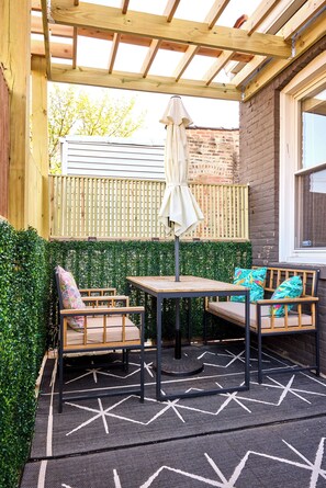 Eine überdachte Terrasse mit Tisch und Stühlen, ein Holzzaun und eine Mauer aus Ziegelsteinen.