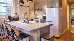 A modern kitchen with a large island, bar stools, stainless steel appliances, and a view of the outside. - A chic second-floor plant-filled retreat in Chicago's Logan Square neighborhood. (Chicago)