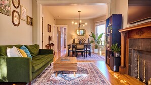 A living room with a green sofa, wooden coffee table, and patterned rug. There is a fireplace, a TV, and a bookshelf. - A chic second-floor plant-filled retreat in Chicago's Logan Square neighborhood. (Chicago)
