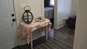 Una habitació amb sòl de fusta, una taula petita amb estovell estampat, un objecte decoratiu i un llit al fons.