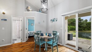 Et spiseområde med et bord og stole, en loftslampe samt udsigt til et udendørs område gennem en skydedør.