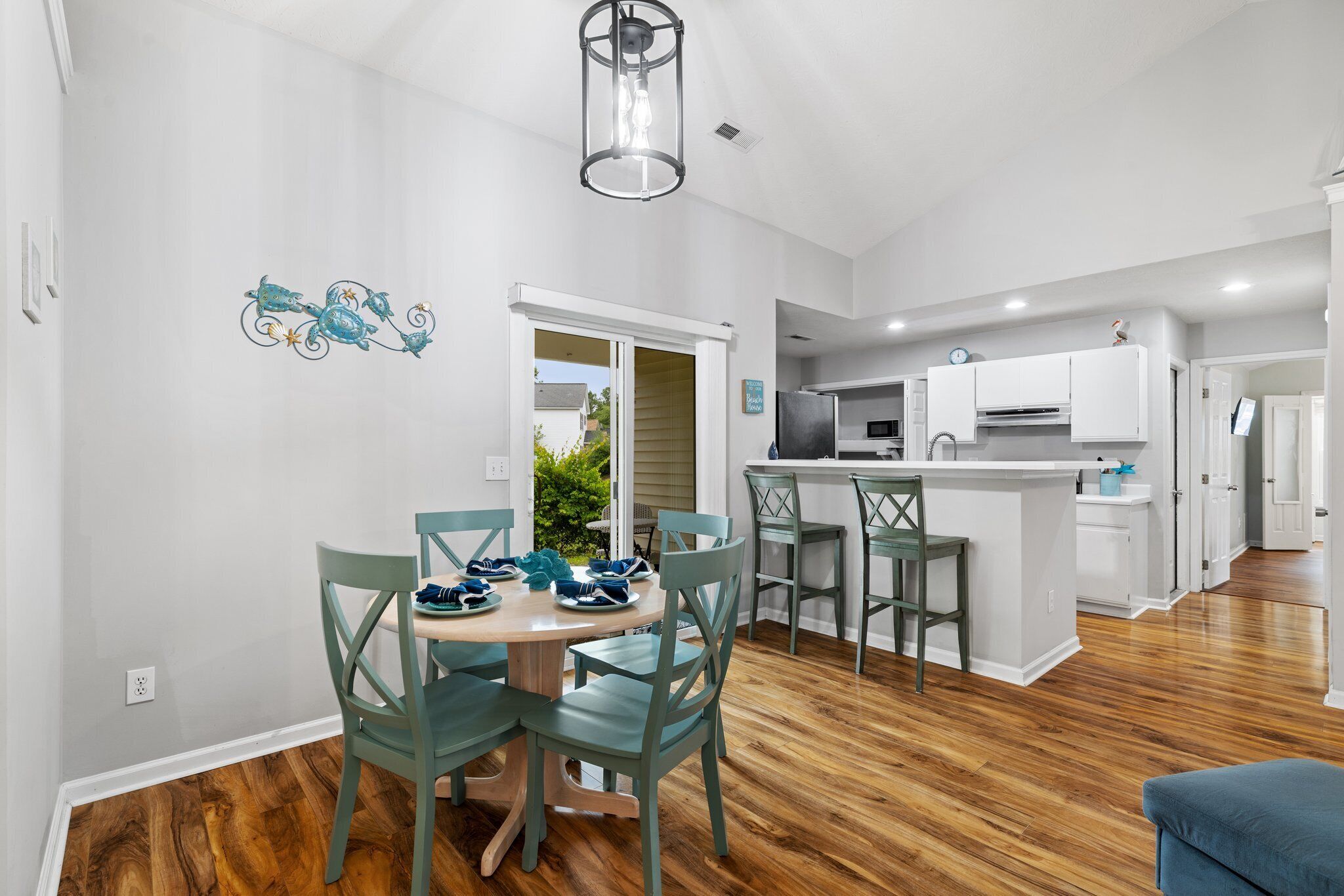 A spacious kitchen with a dining area, wooden flooring, and teal chairs.