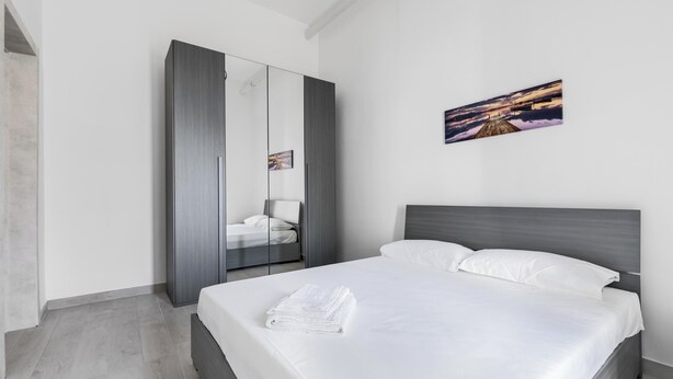 Een moderne slaapkamer met een groot bed, een kledingkast en een schilderij aan de muur.