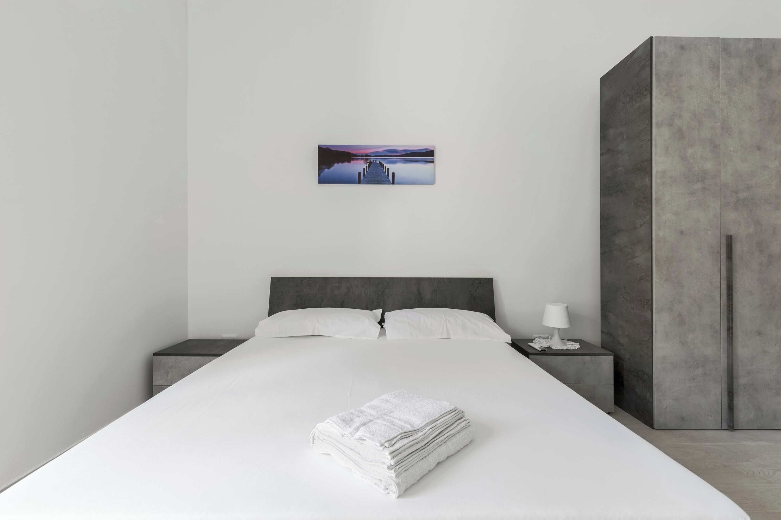 A modern bedroom with a large bed, a nightstand, a bedside table, and a wardrobe.
