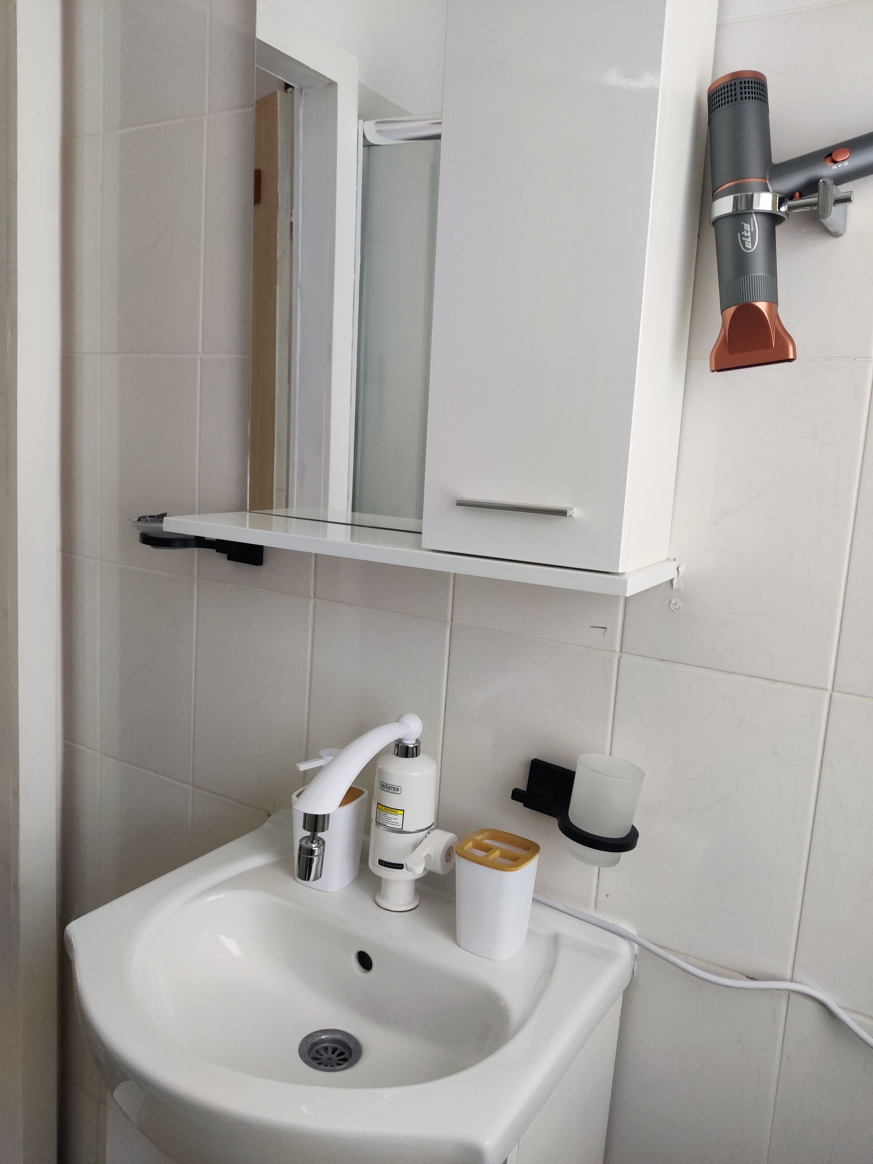 A bathroom with a white sink, a mirror, a cabinet, and a hairdryer mounted on the wall.