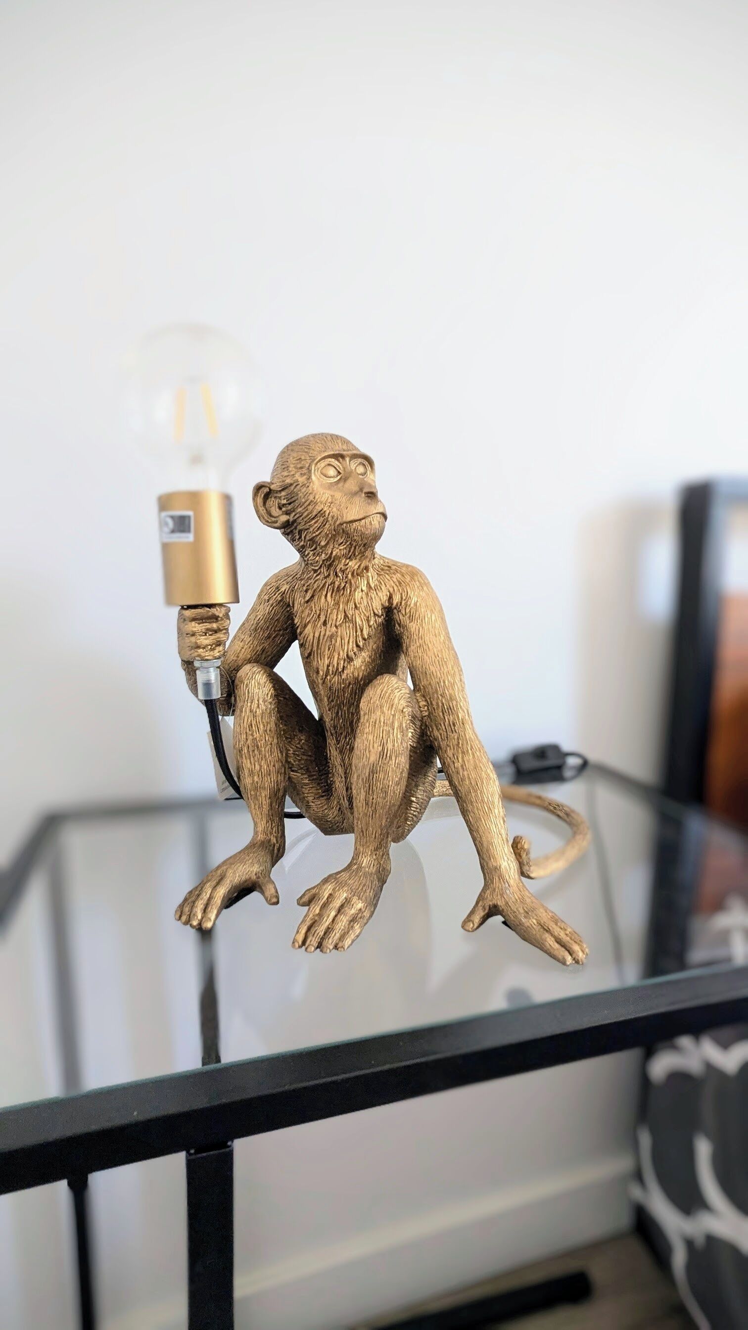 A glass table with a bronze monkey sculpture holding a light bulb.