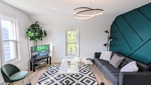 A modern living room with a TV on a stand, a sofa, a coffee table, and a large window.