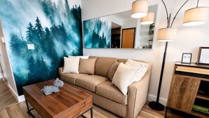 A living room with a sofa, a wooden coffee table, a painting of a forest, and a mirror. - ES326 Super Cute Village Studio Condo Slope View (Snowshoe)