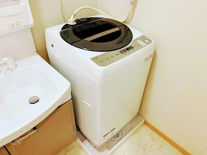 Une petite machine à laver blanche, fixée au mur, dotée d’un panneau de commande, et placée à côté d’un lavabo blanc dans une petite salle de bain.