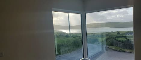A room with a large sliding glass door leading to a balcony with a view of a lake and hills.