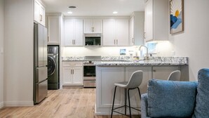 A modern kitchen with white cabinets, a central island with bar stools, a stainless steel refrigerator, and a microwave. - The Square Unit 2, Cozy 1 BR by VelvetDitchVillas (Oxford)