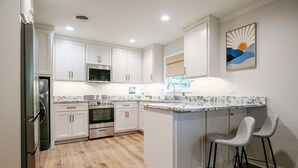 A modern kitchen with white cabinets, a granite countertop, stainless steel appliances, and a bar area with two stools. - The Square Unit 2, Cozy 1 BR by VelvetDitchVillas (Oxford)