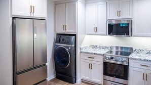 A modern kitchen with white cabinets, a stainless steel refrigerator, a washing machine, a microwave, and an oven. - The Square Unit 2, Cozy 1 BR by VelvetDitchVillas (Oxford)